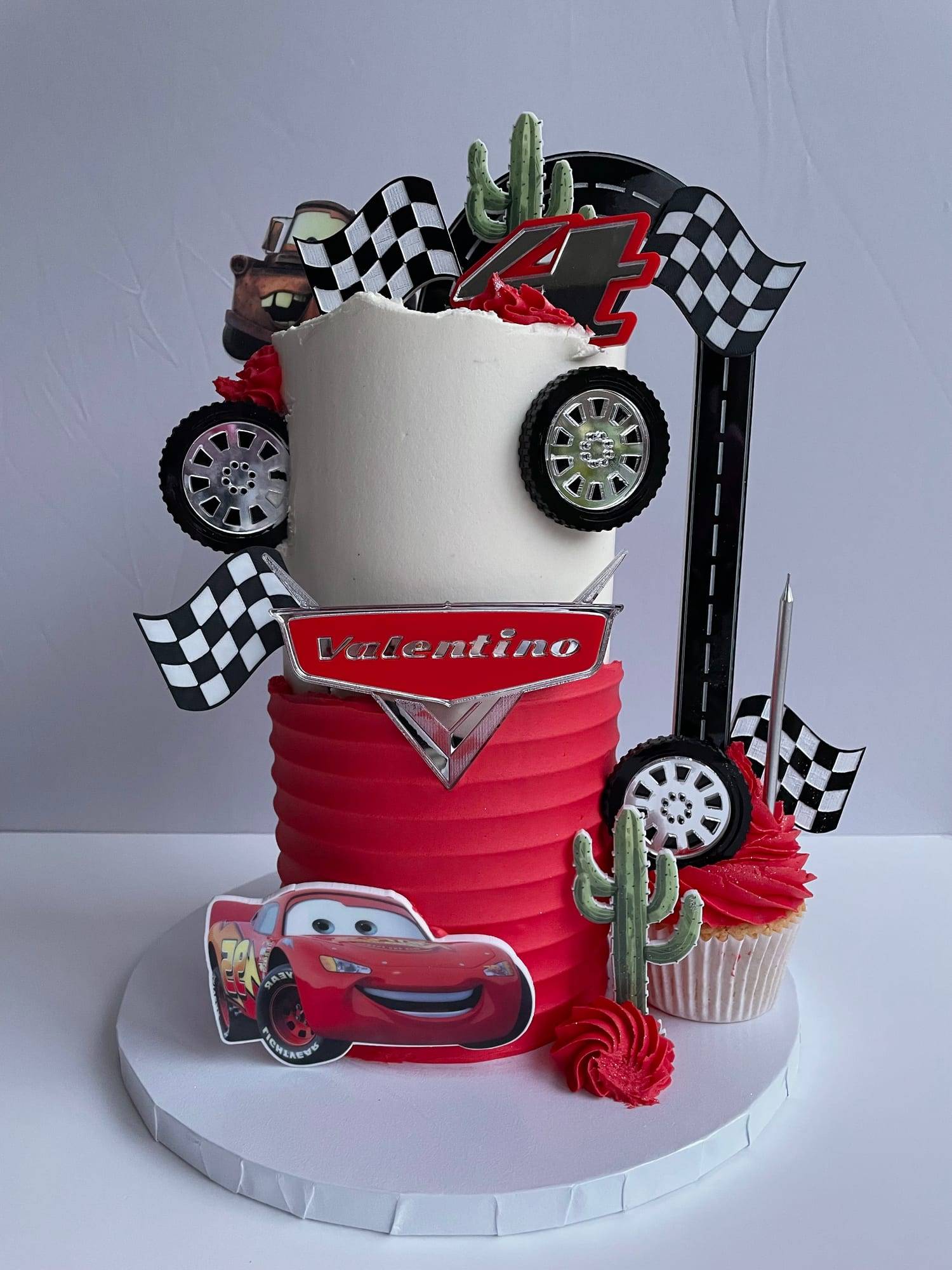 Cars-themed birthday cake with white and red buttercream, toy wheels and a personalised chrome number plaque