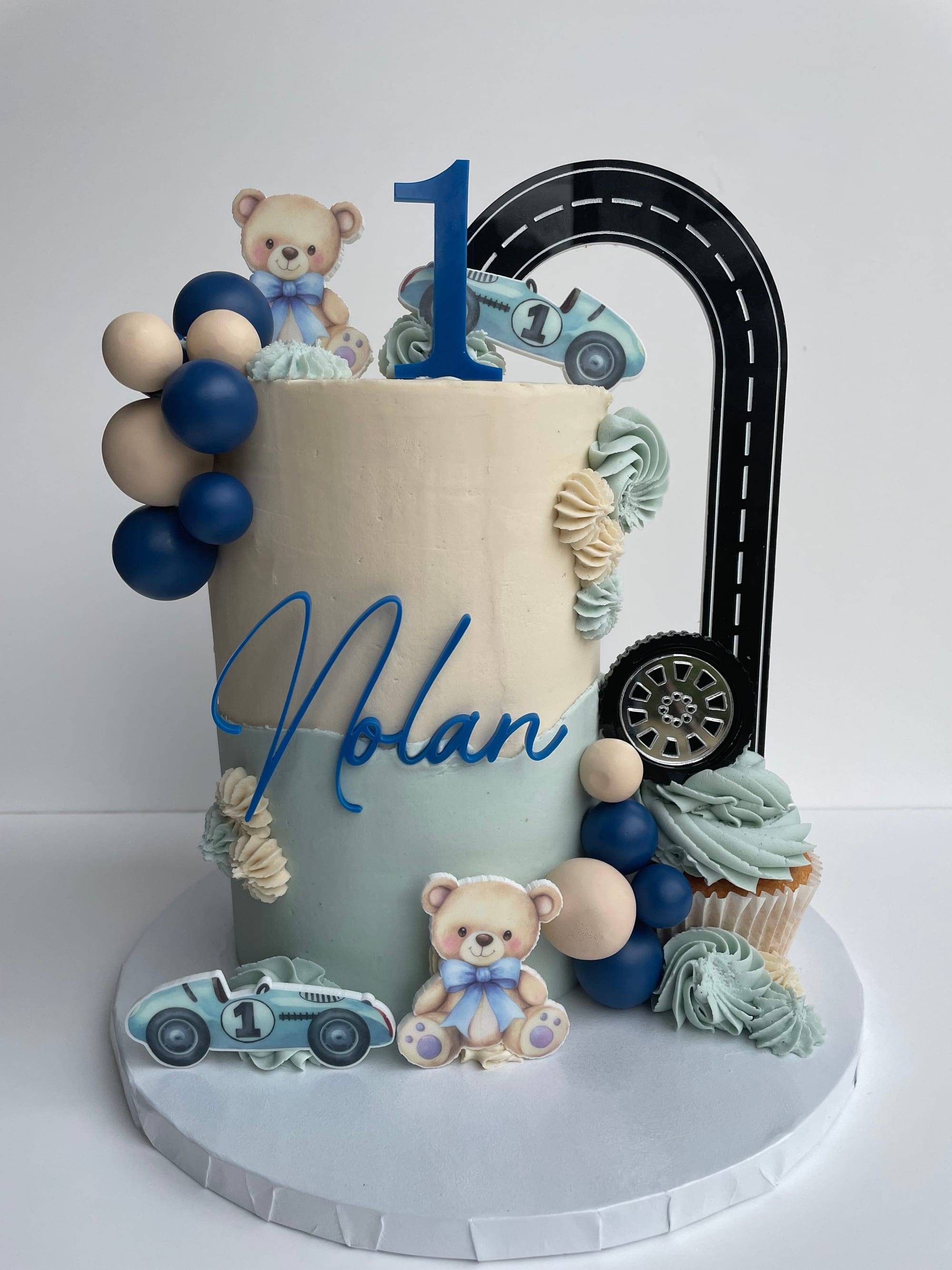 1st birthday cake with cream and sage buttercream, a road-shaped number-one topper and a matching cupcake