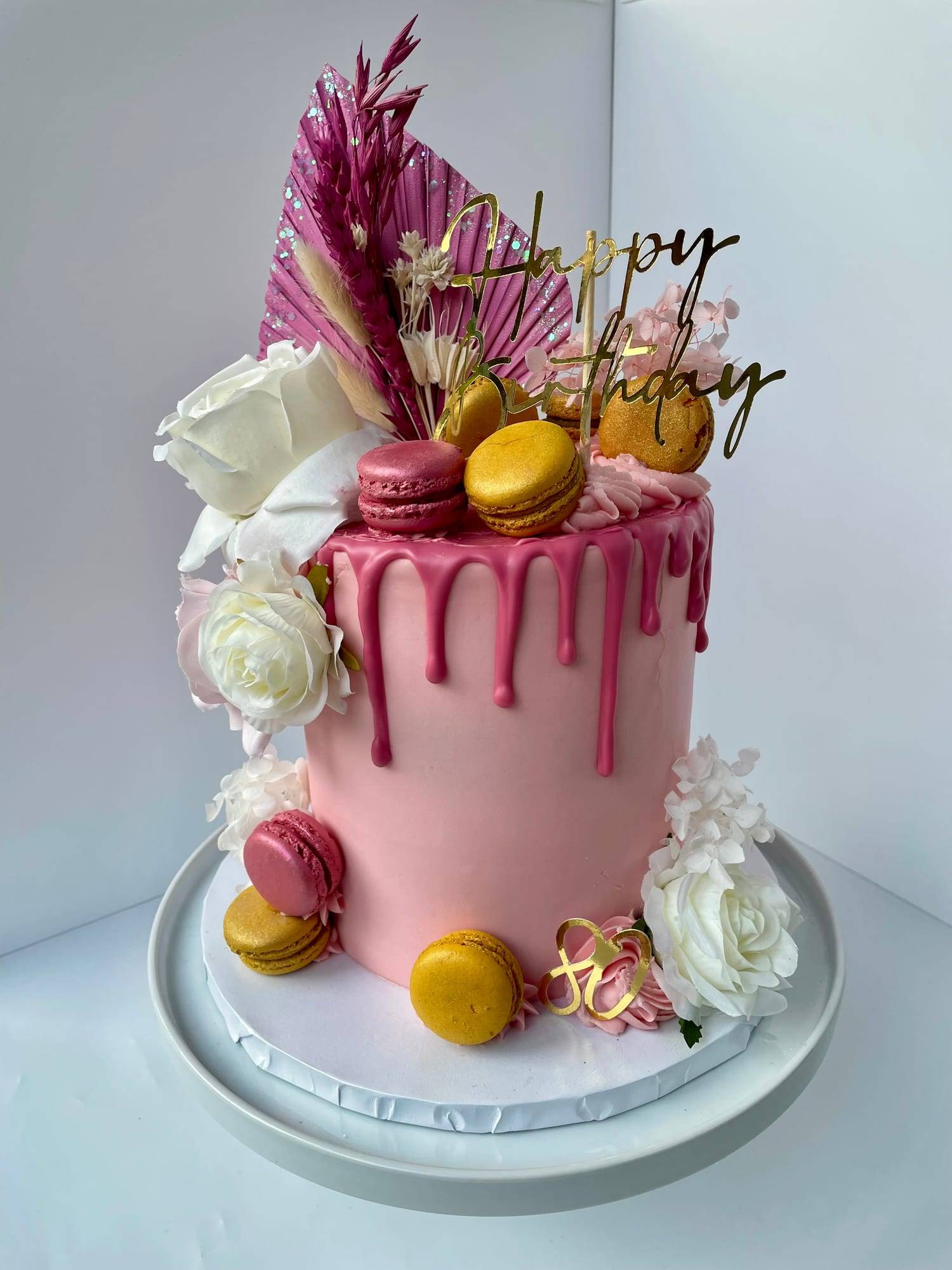 80th birthday drip cake in pink buttercream with macarons, dried palm fronds and fresh roses