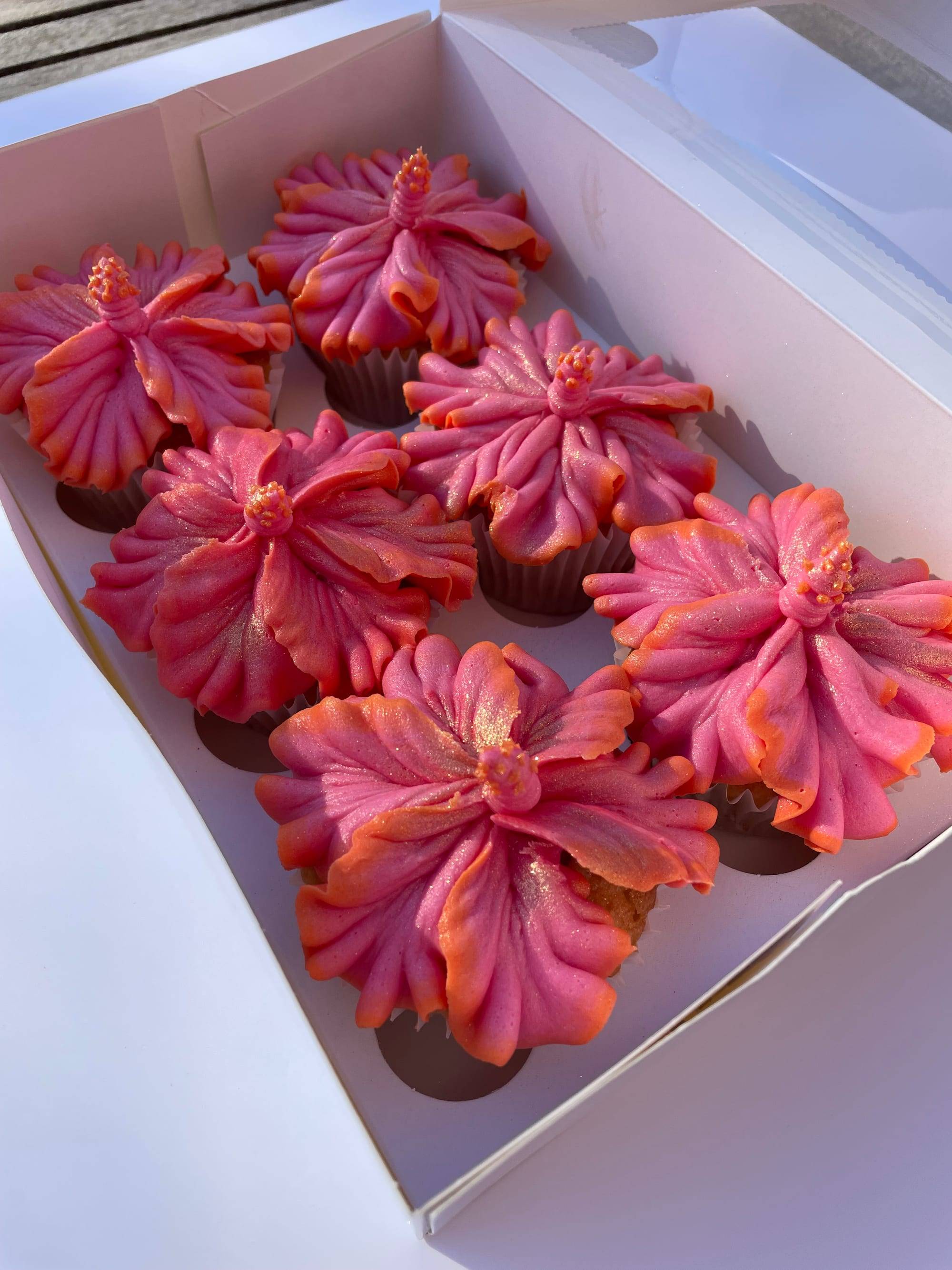 Tropical hibiscus flower cupcakes piped in coral-to-pink ombre buttercream with gold shimmer