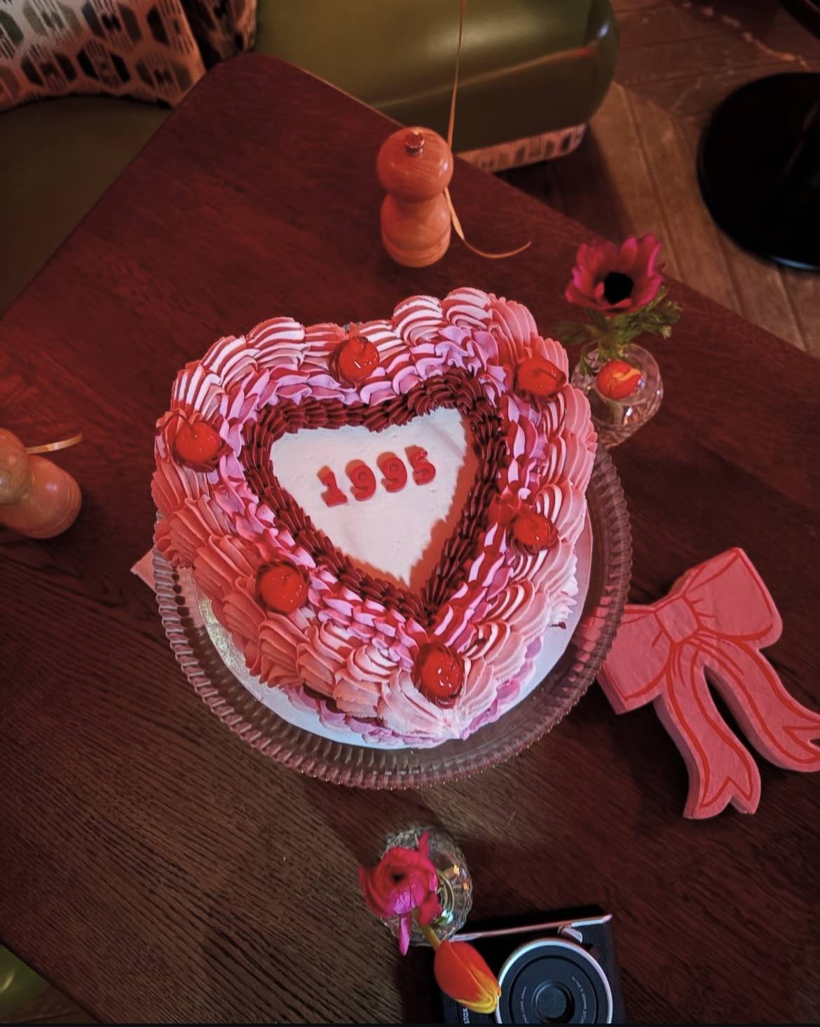 Heart-shaped anniversary cake styled on a table with pink-to-burgundy ombre shell piping and glacé cherries, marking 1995