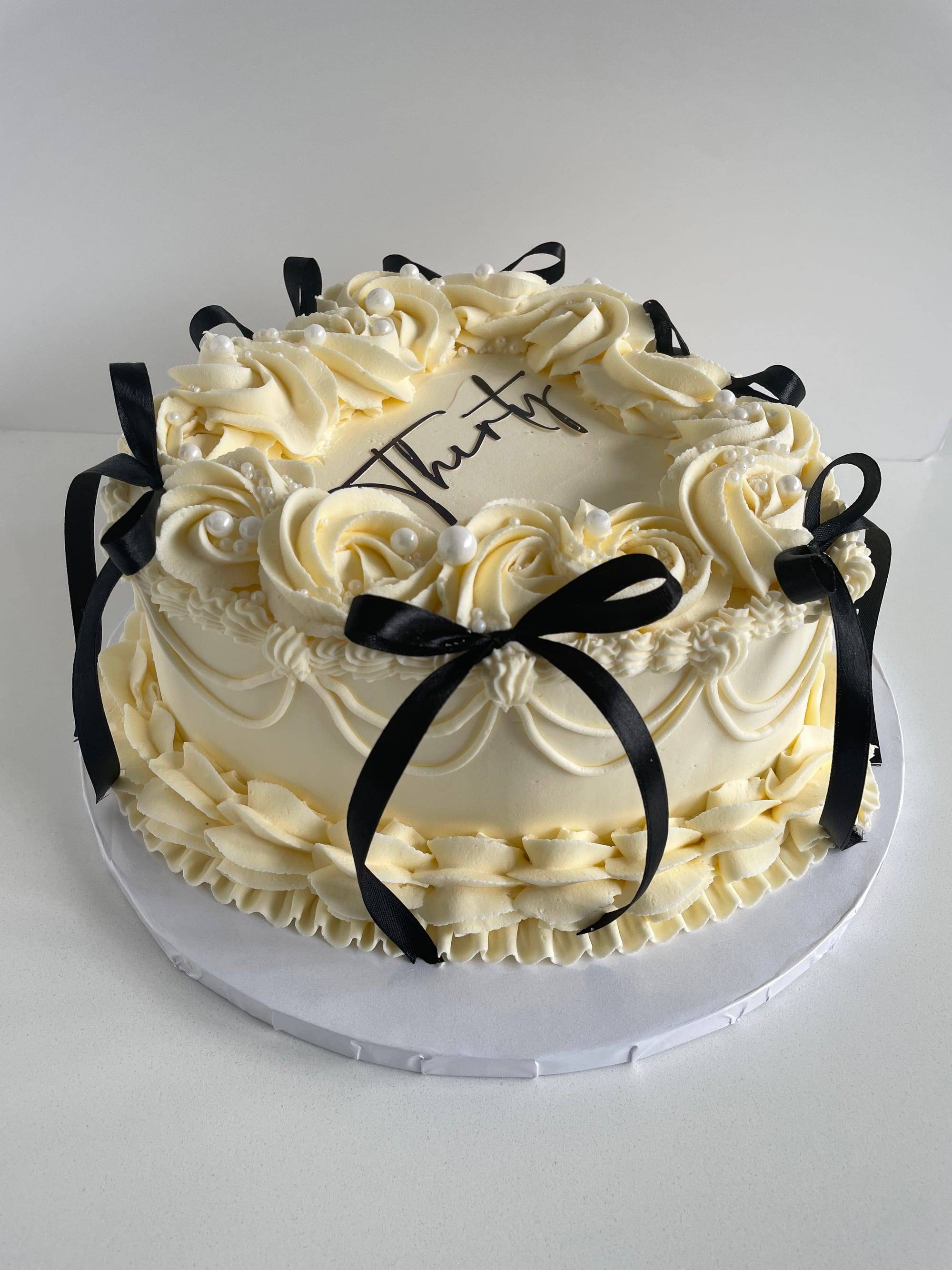 Two-tier heart-shaped 30th birthday cake with ivory rosette buttercream, black ribbon bows and pearls